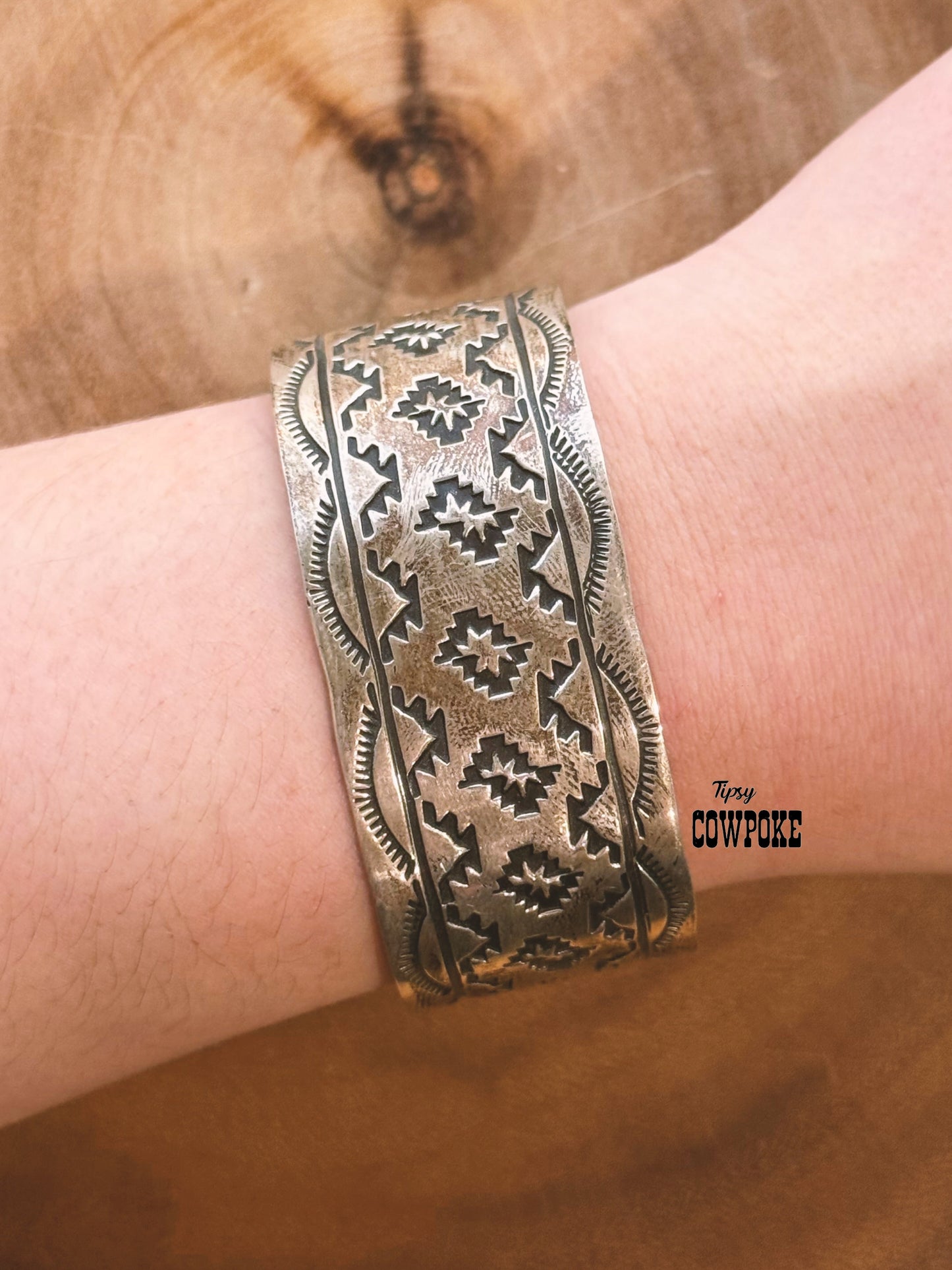 Bronze patterned cuff bracelet on a wrist with a wooden background