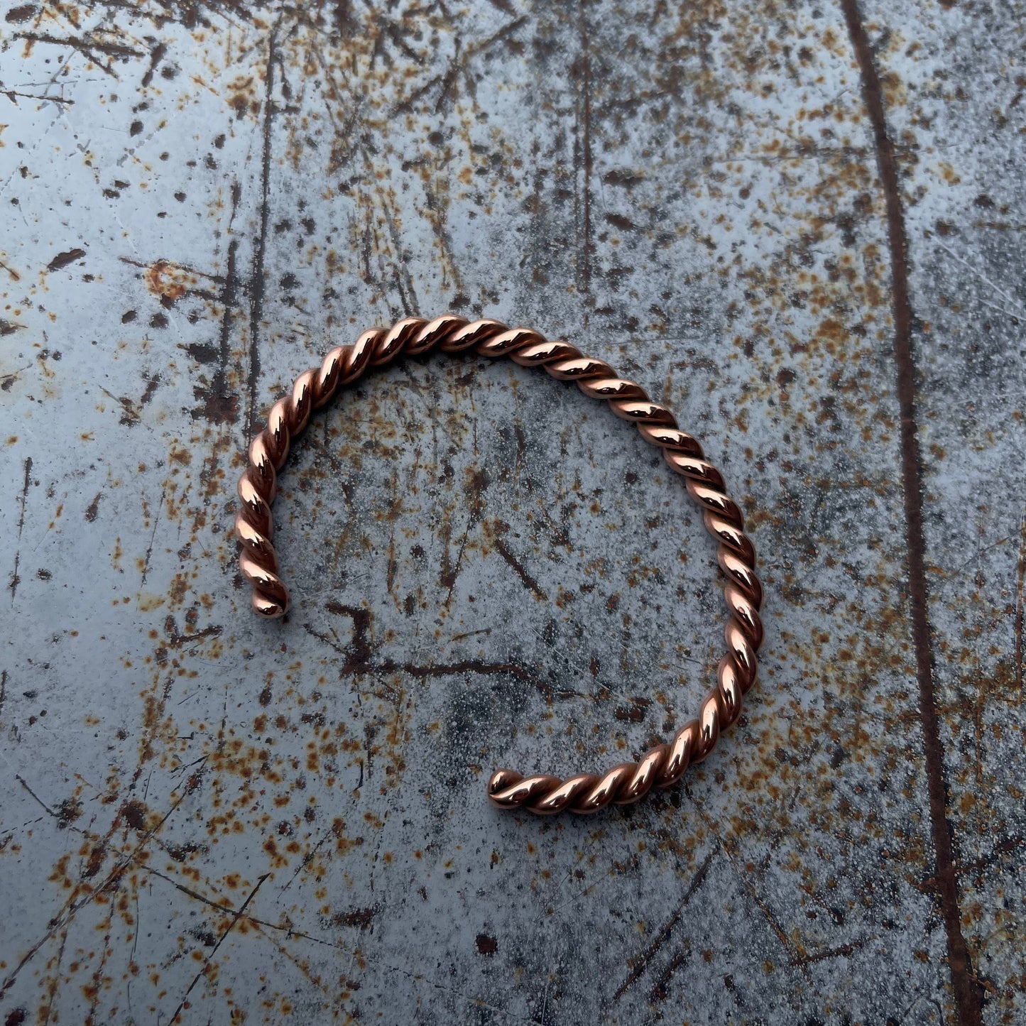 Copper hoop bracelet on a textured metal surface