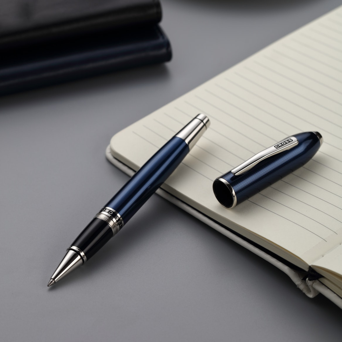 Blue pen with silver accents on a gray surface next to an open notebook