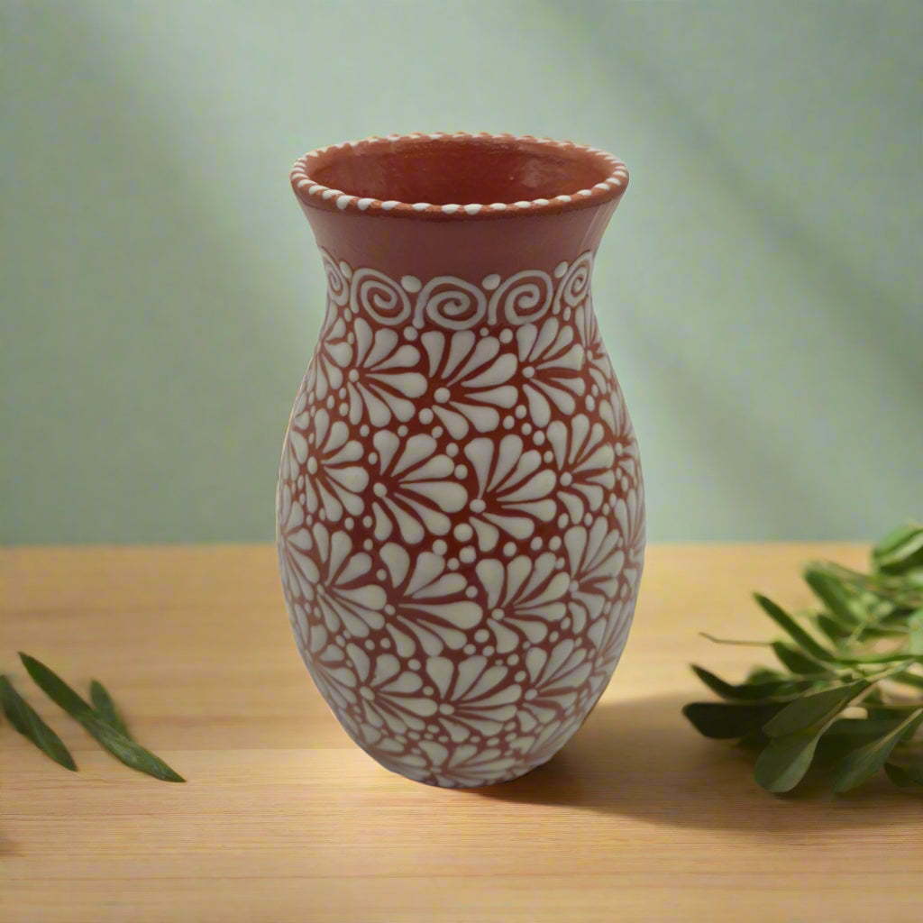 Ceramic vase with white floral patterns on a wooden surface with a green background