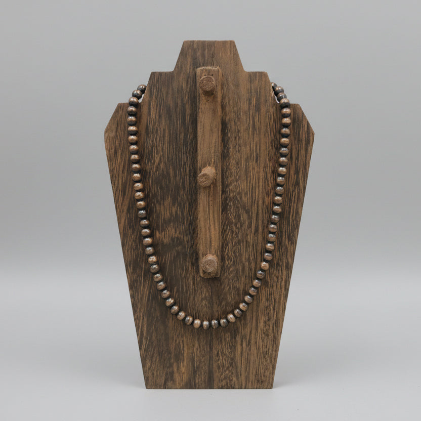 Wooden necklace stand with a beaded necklace on a wooden surface