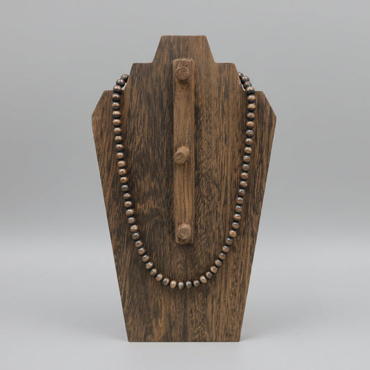 Wooden necklace stand with a beaded necklace on a wooden surface
