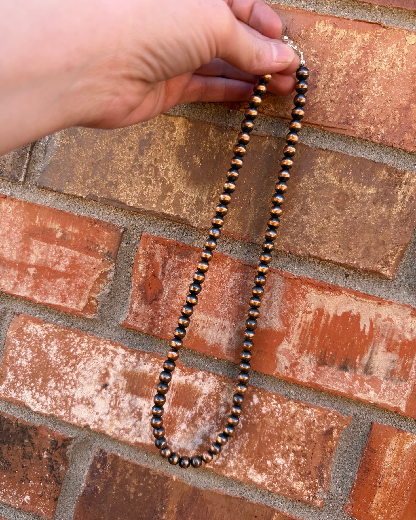 Necklace with black beads held against a brick wall