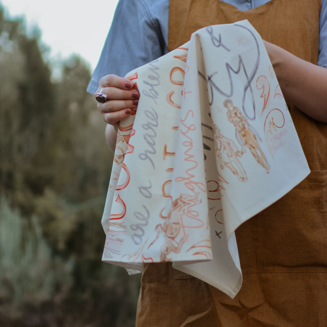 Person holding a printed tea towel with printed designs outdoors