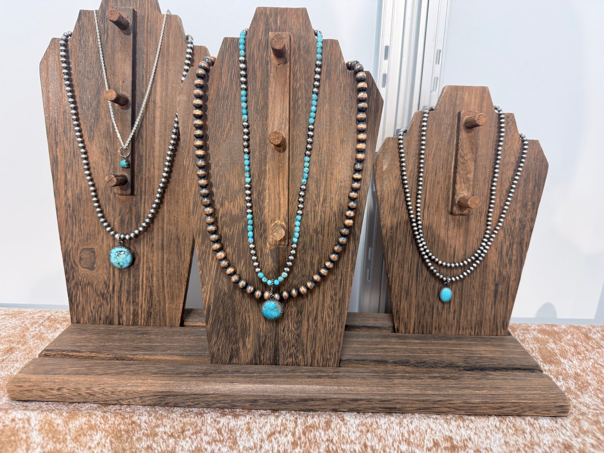 Three necklaces on wooden stands with a neutral background