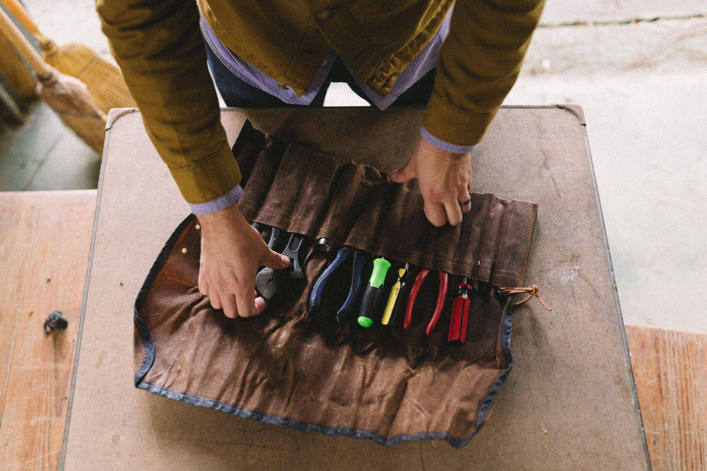 Person organizing tools in a brown leather roll on a wooden surface.