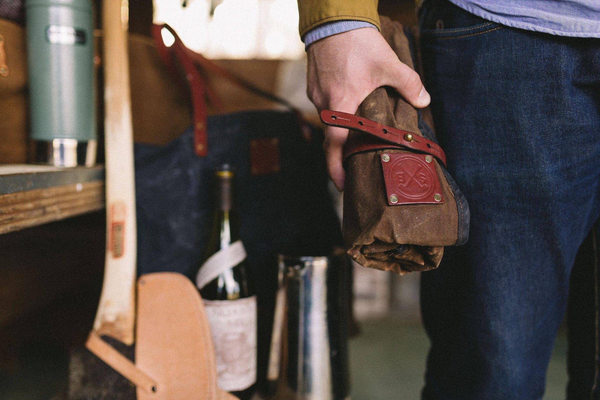 Person holding a leather tool roll with a blurred background of a workshop.
