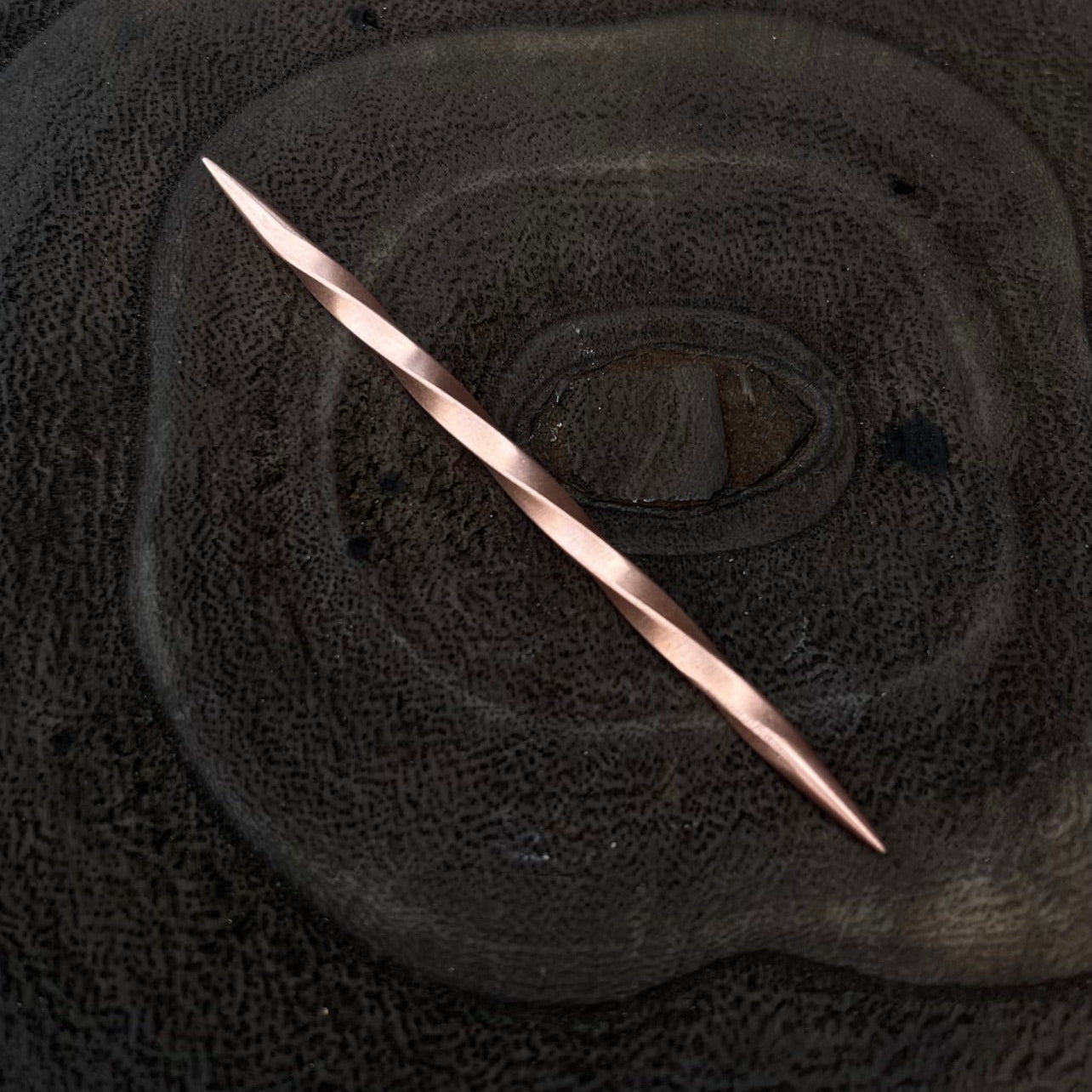 Close-up of a textured black surface with a copper toothpick.