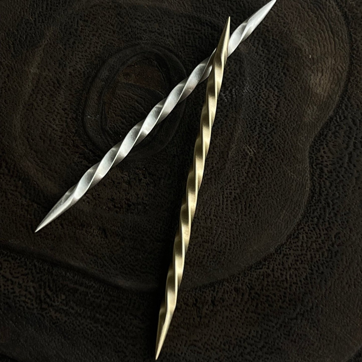 Two metallic toothpicks, one silver and one gold, on a textured black surface.
