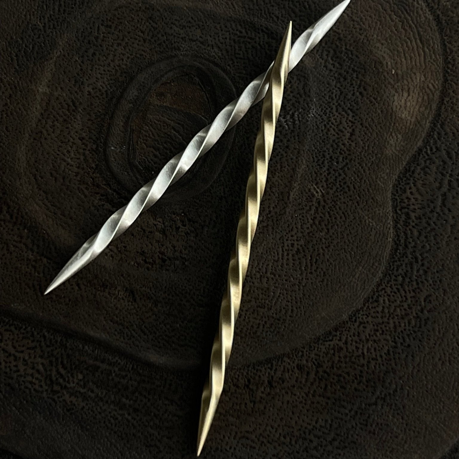 Two metallic toothpicks, one silver and one gold, on a textured black surface.