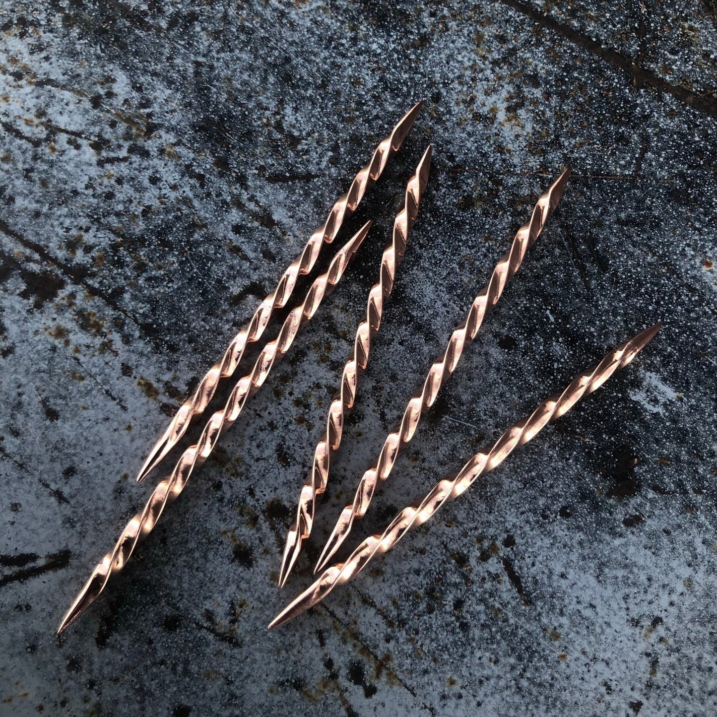 Three rose gold toothpicks on a textured gray surface