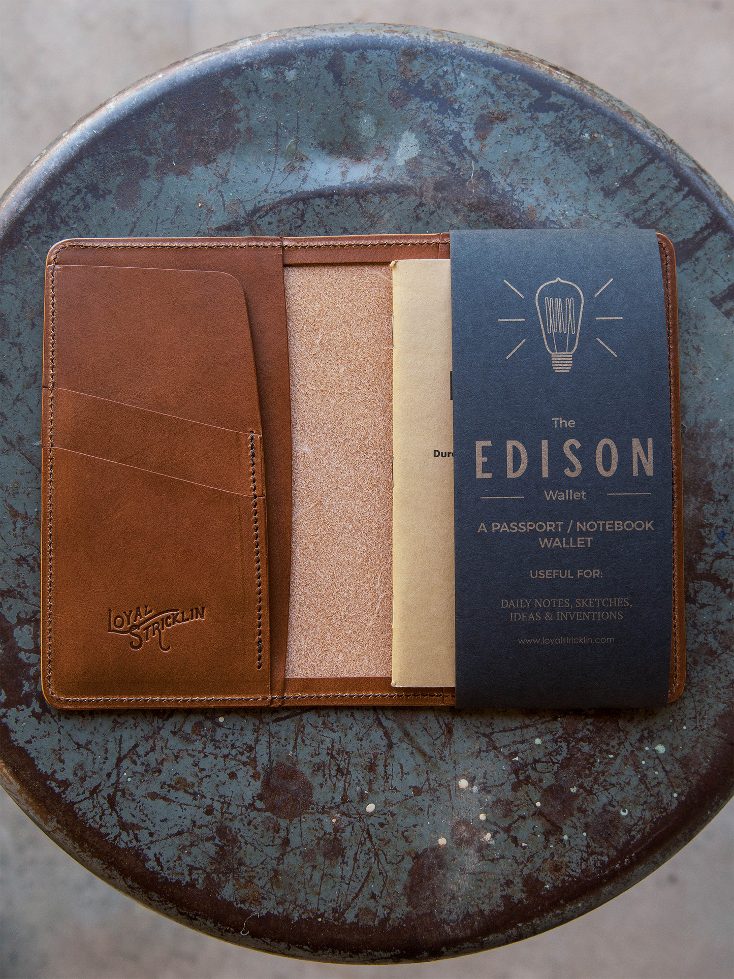 Brown leather wallet with beige interior on a blue textured surface, featuring 'The Edison' branding.