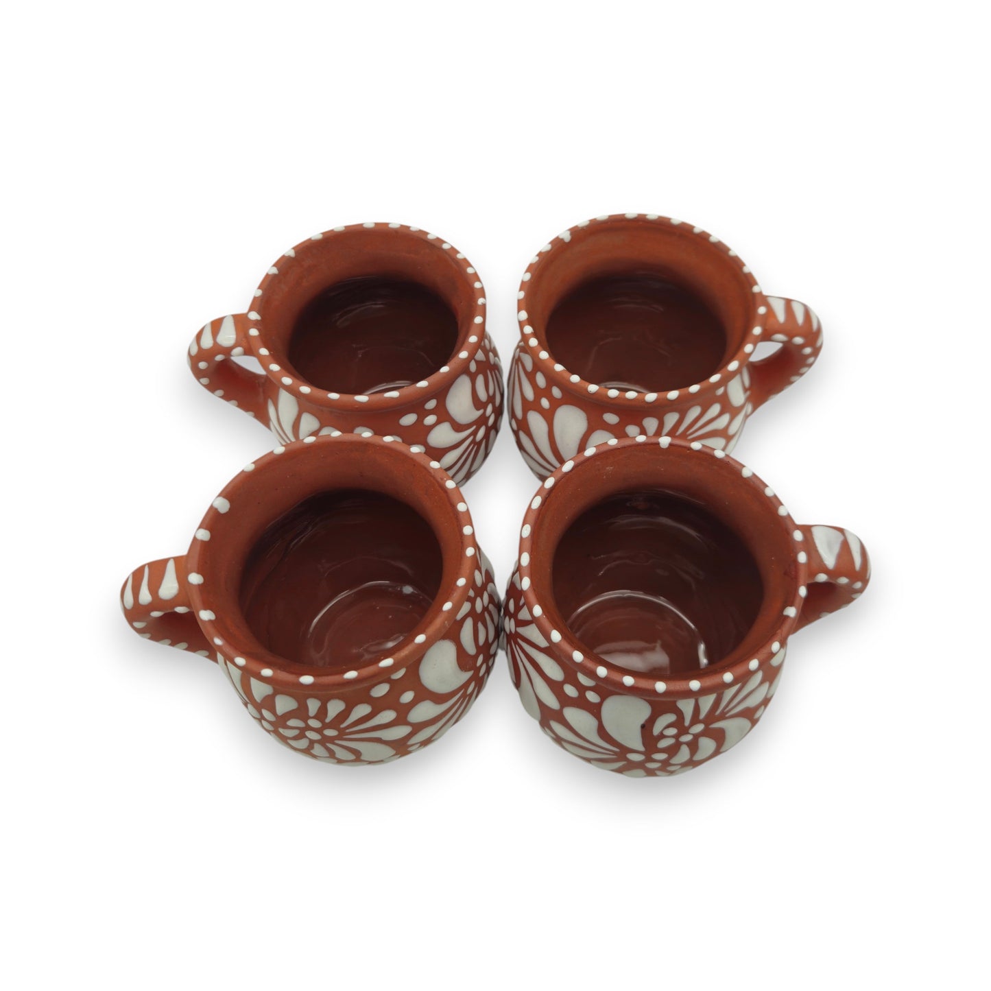 Four terracotta cups with white floral patterns on a white background