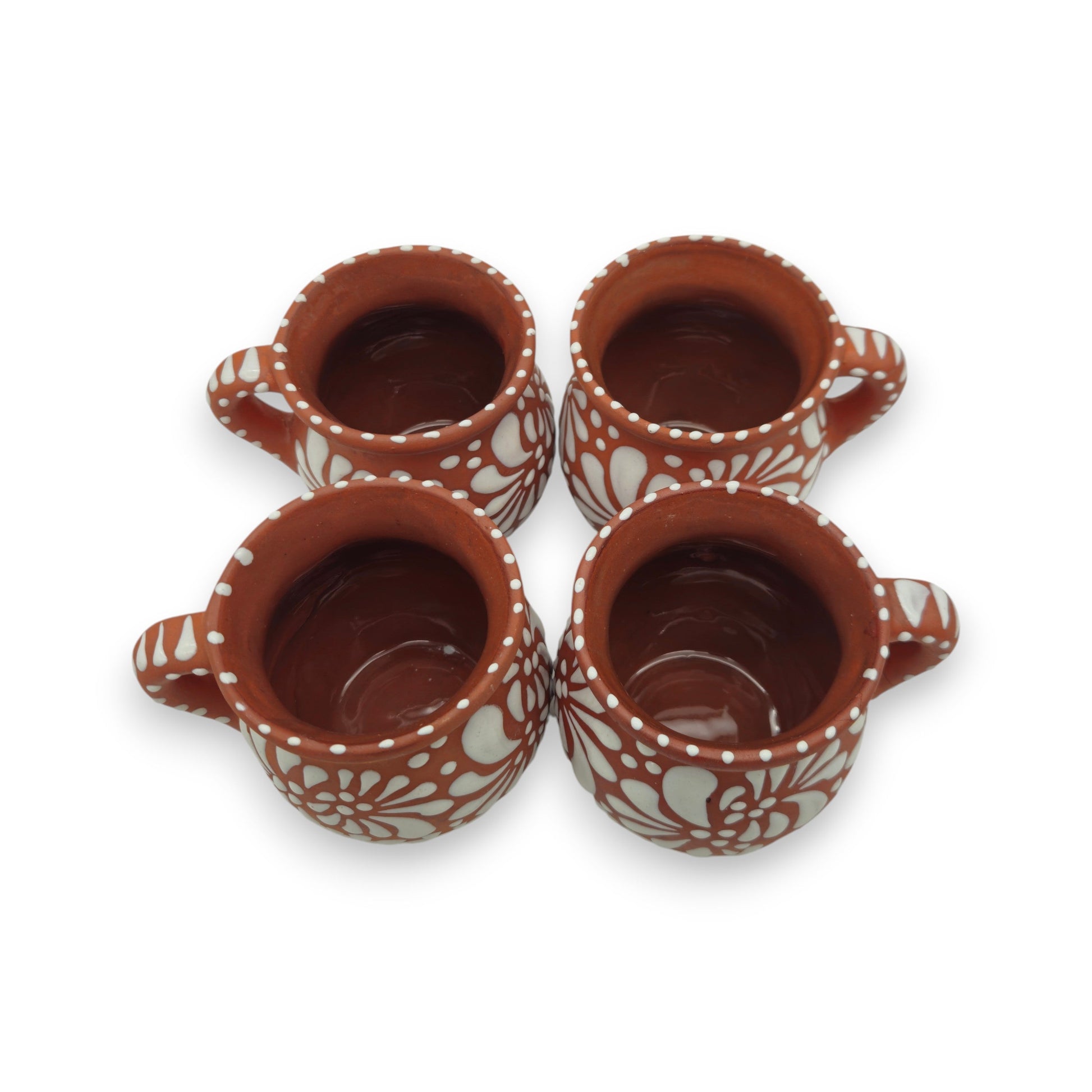 Four terracotta cups with white floral patterns on a white background