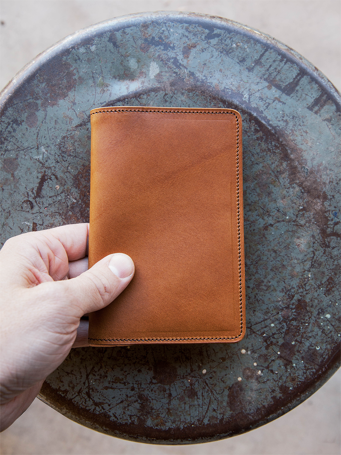 Brown leather wallet held by a hand on a rustic metal surface